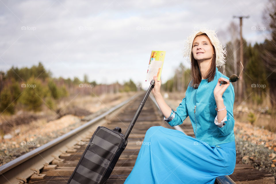 Mid adult woman sitting on railway track with her luggage