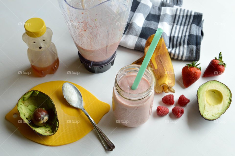 Fresh fruit smoothie in a glass with banana peel, avocado, strawberries, raspberries, and honey bear