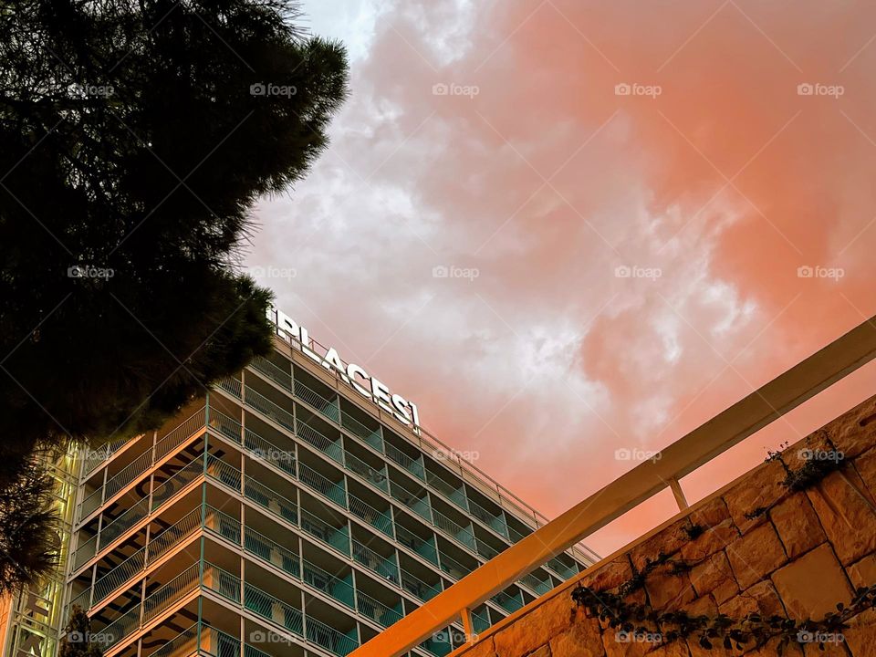 Dramatic twilight sky with sunset coloured pink clouds with geometrical shape Places hotel, dark trees and stone wall under