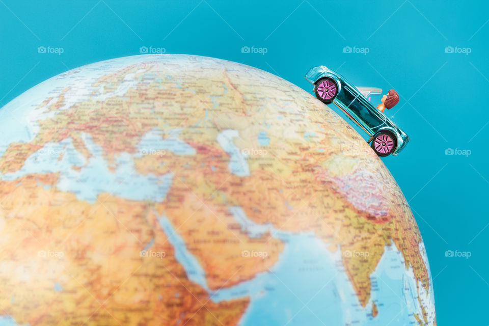 Toy car on the globe on plain blue background