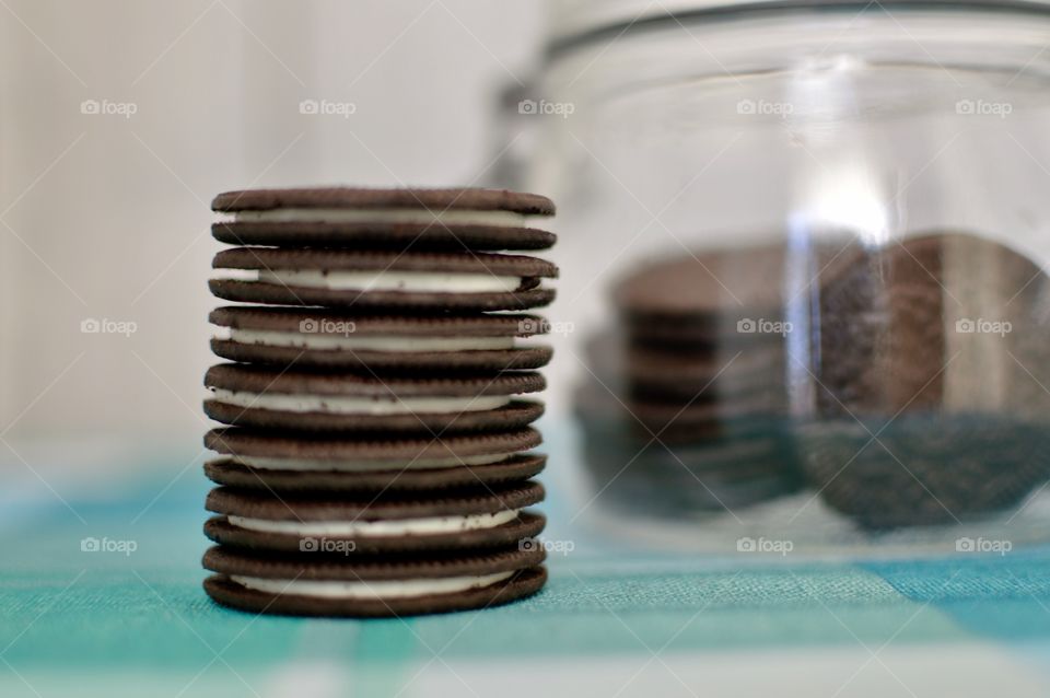 A stack of Oreo cookie thins in front on a glass jar on  a white background 