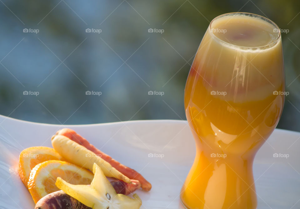 Making homemade fresh orange, carrot and tropical carambola juice with  ingredients and smoothie on platter outdoors in summertime sun for healthy refreshing drink 