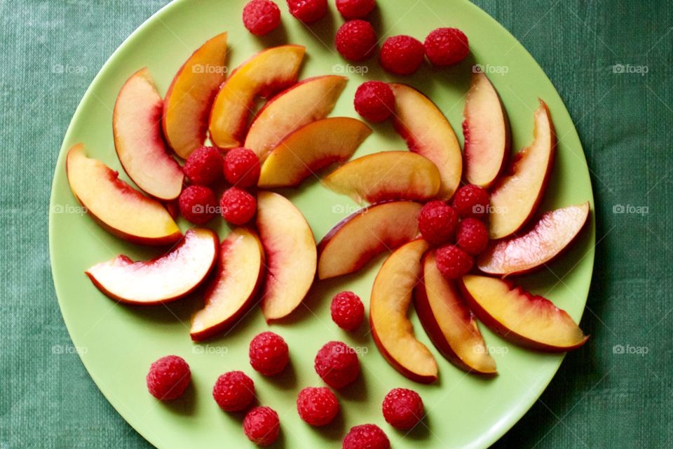 Flat lay of decorative arrangement of fresh nectarine slices and raspberries on a green plate with green background 