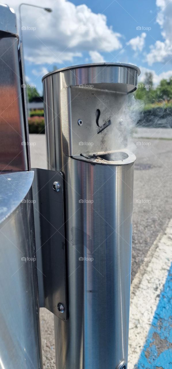 Smoke rising from inside metal cigarette disposal bin caught on fire.