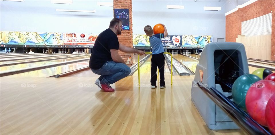 dad helps the kid play bowling