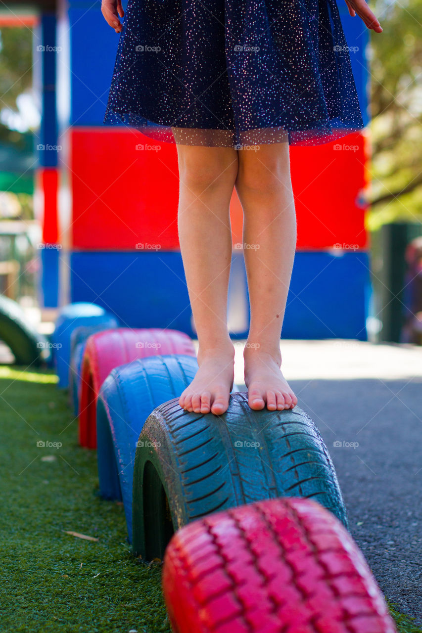 Little girl playing on old painted and recycled car tires on a playground. Looking after the earth starts with recycling and upcycling.