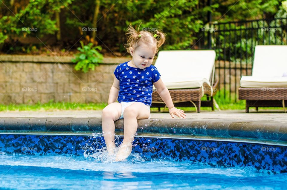 Cute little girl sitting by swimming pool splashing water