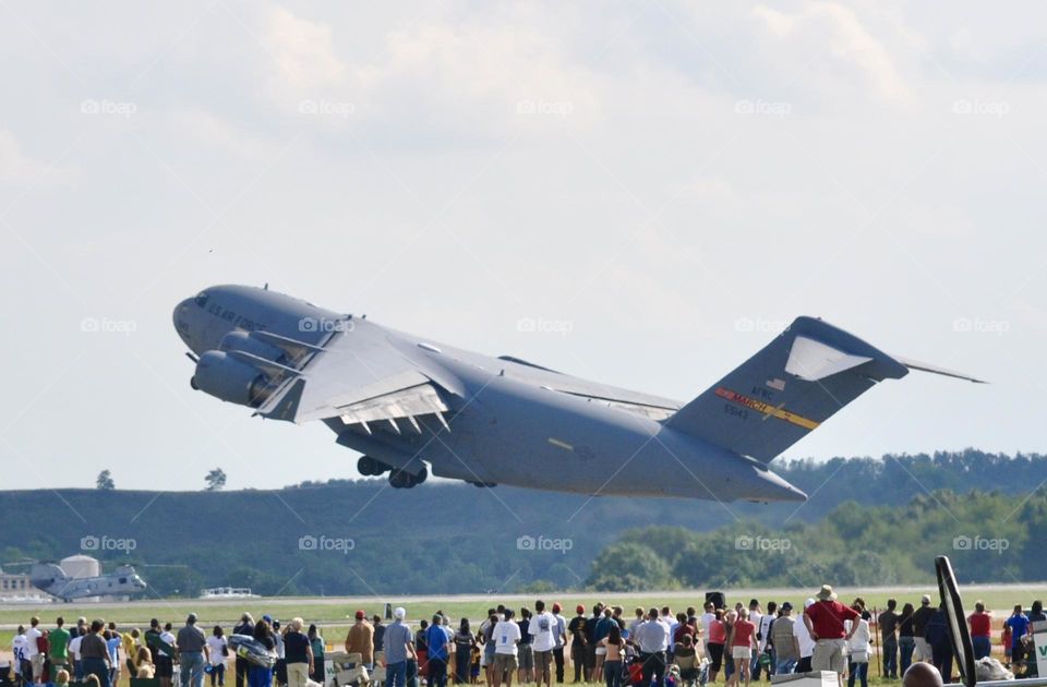 A crowd of people watching a large military plane take off