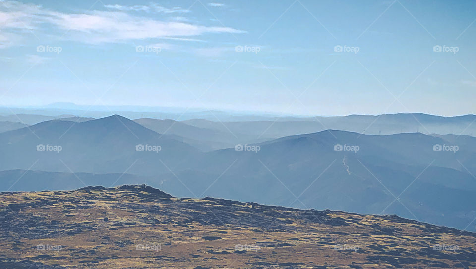 The peaks of mountains and hills poke out of the clouds in this hazy landscape view