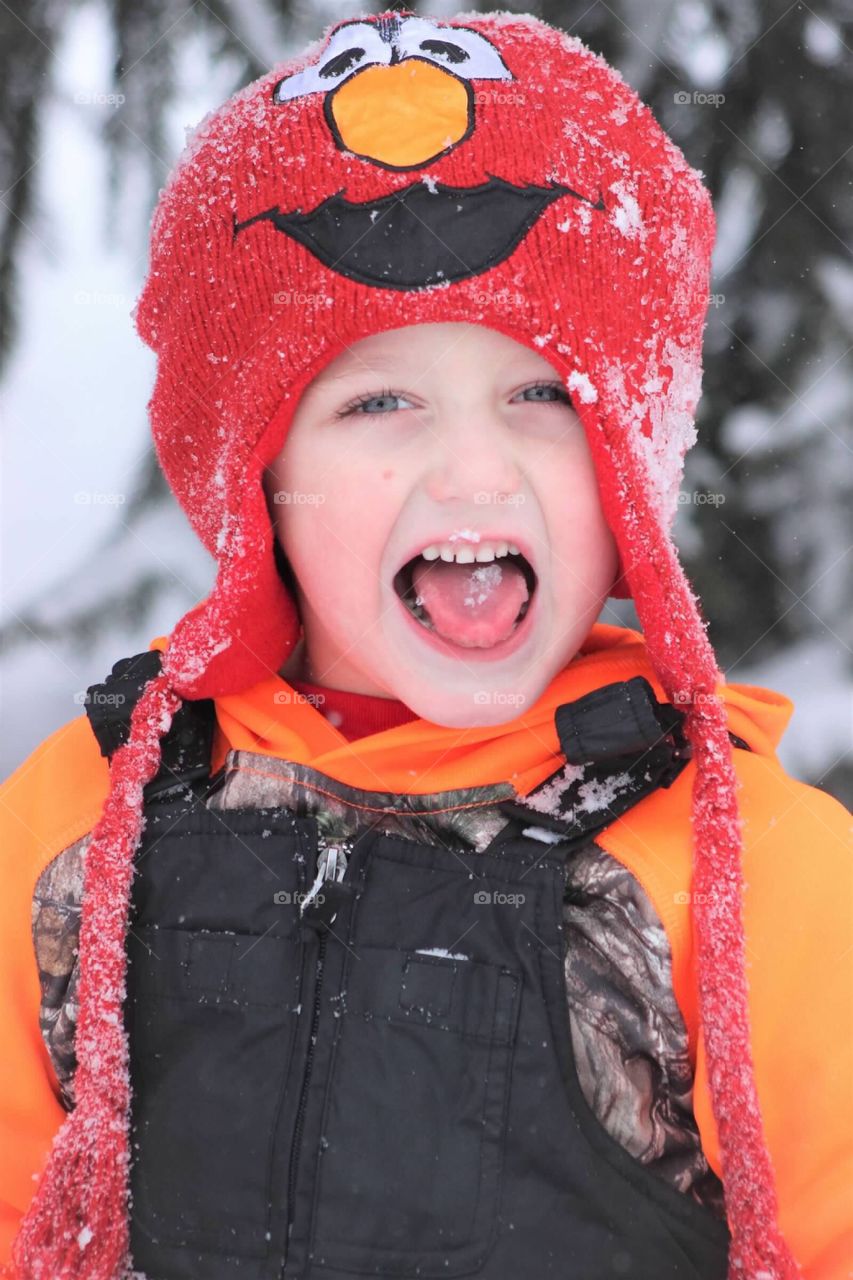 I mischievous little boy bundled up playing in the snow, catching a flake on his tongue. 