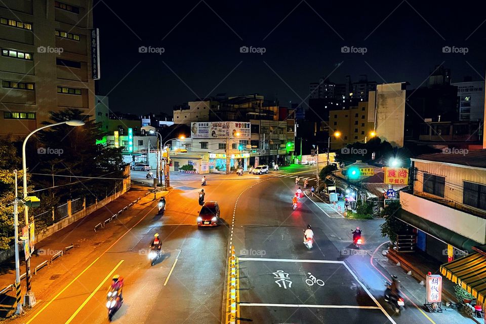 A busy intersection at nighttime in Changhua, Taiwan. There are buildings in the distance, and to both sides. 