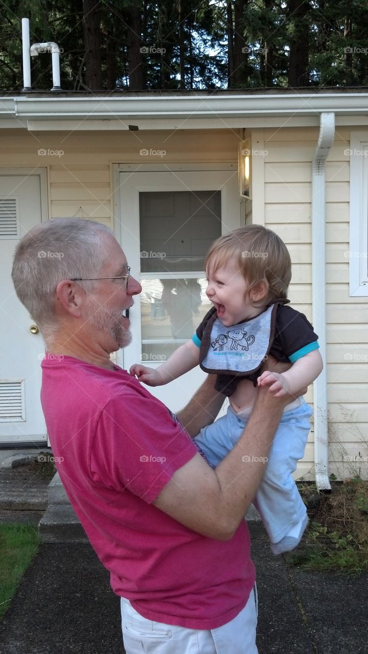 Senior man holding grandson in front of house