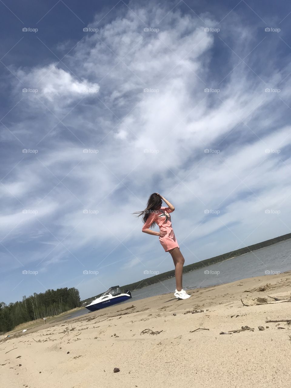 The figure of a girl against the blue sky. Girl on the beach sea with a yacht. Clouds in the sky. Nature in Siberia. 