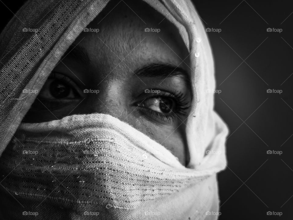 Black and white portrait of a woman wearing a white scarf over her head and across her mouth to protect against covid19.