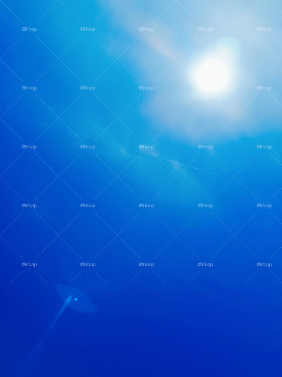 Low angle view to the sun on a blue and nearly cloudless sky