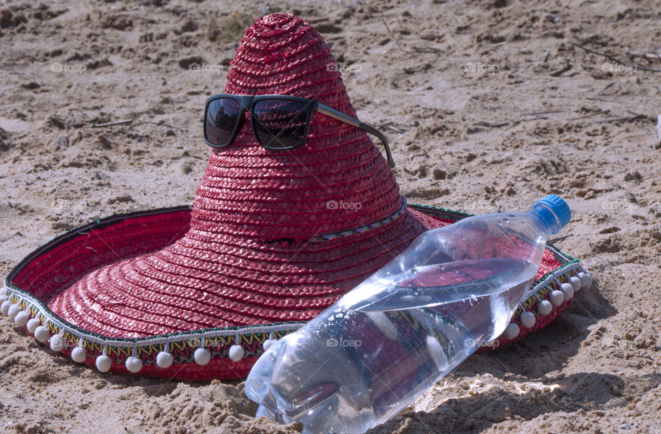 Hat of a sombrero and a bottle of drinking water lies on the beach