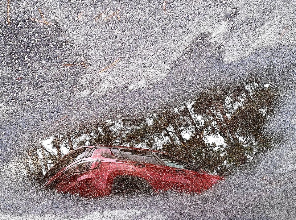 rainy days reflection of Jeep Compass the sky and woods in a rain puddle on the asphalt road way