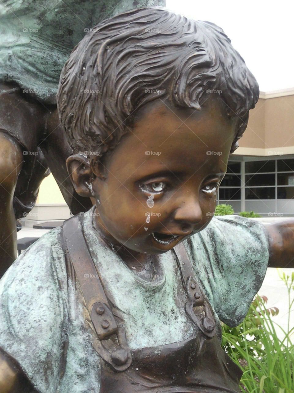 Bronze statue of happy child with ironic patina tears.