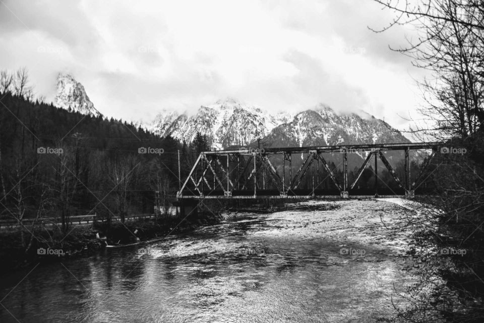 vintage railway bridge over a river with snowcapped mountains