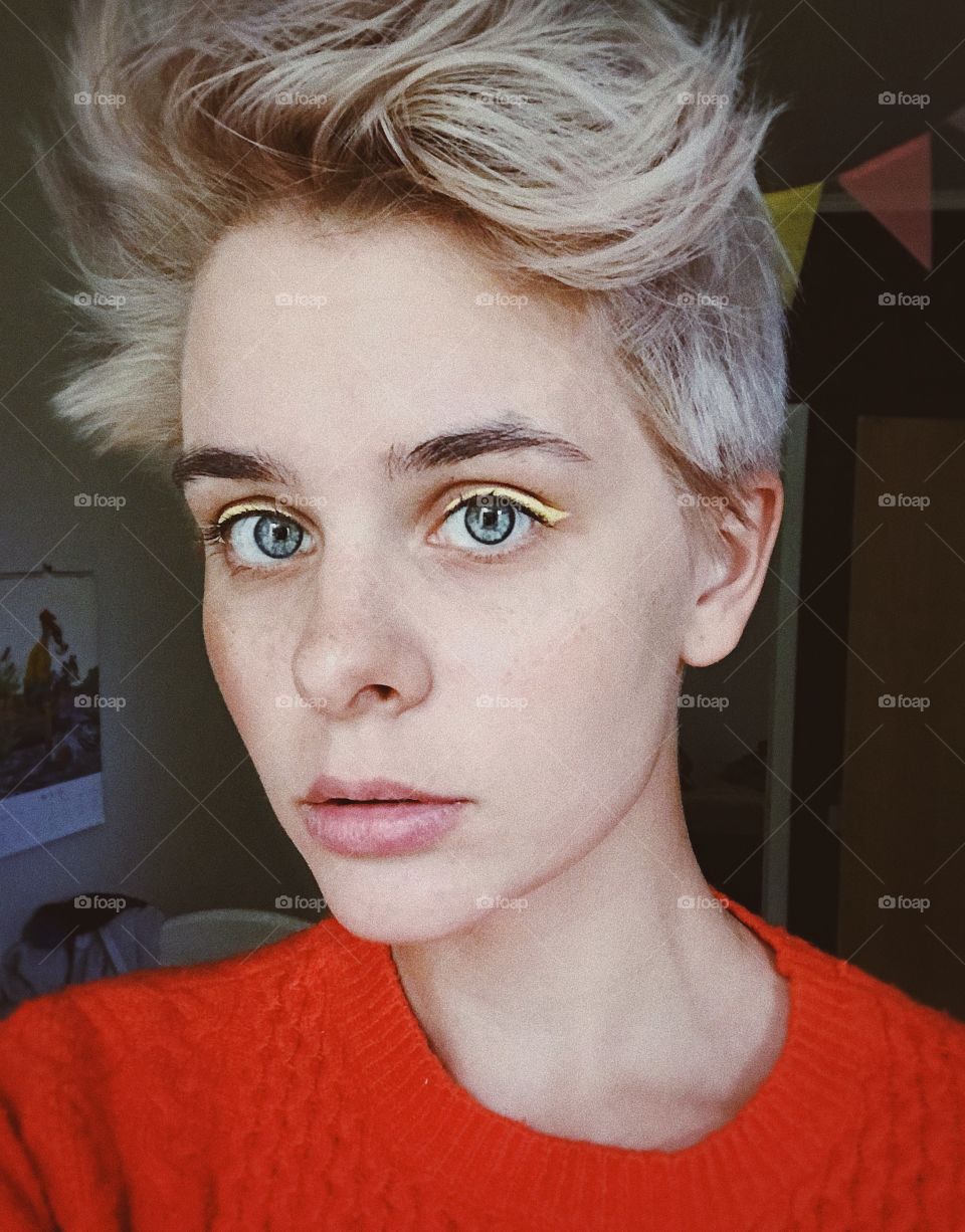 Selfie portrait of young short haired blond woman with freckles and yellow eyeliner 