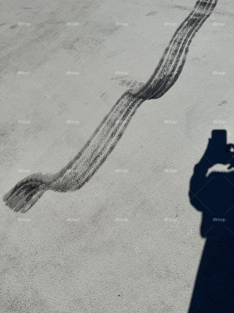 Shadow self portrait with iPhone taking a picture of tire skid marks on light colored parking structure surface