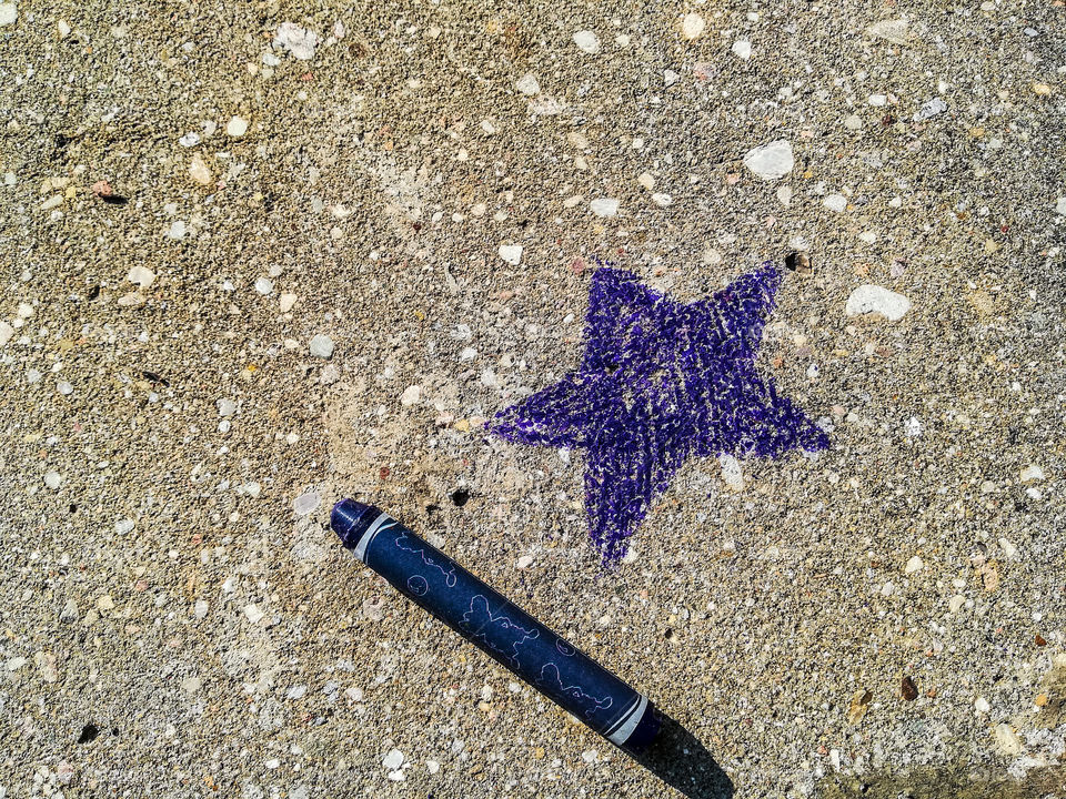 Purple star drawn on the pavement with purple colored wax crayon; summertime, graffiti