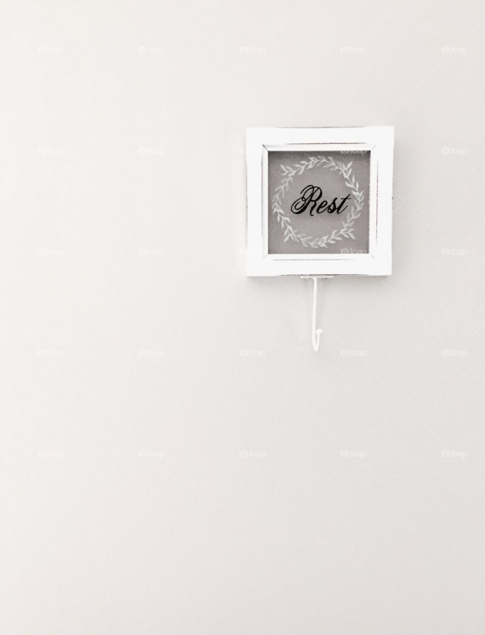 "Rest" - glass and wood plaque with hook and  the word "Rest" painted in black cursive lettering with a white laurel wreath around it on a neutral-colored wall