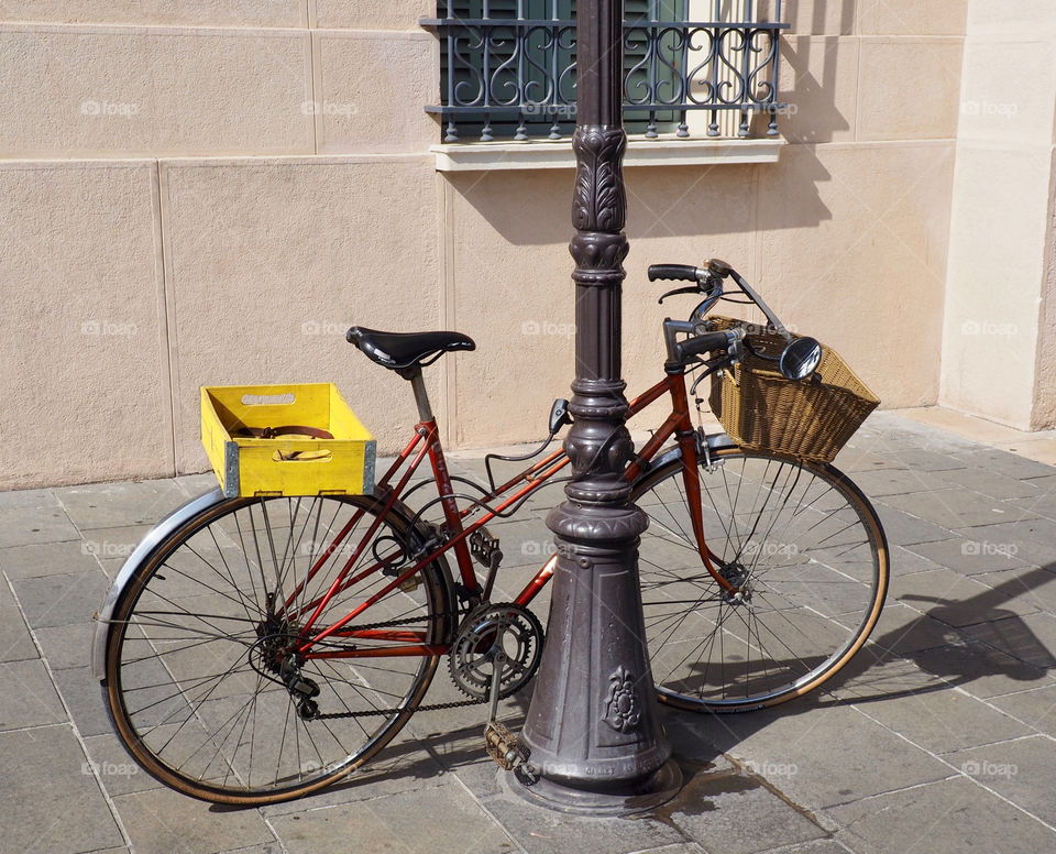 Classic red bicycle with yellow crate  basket attached to lamppost in the old town of Nice, France.