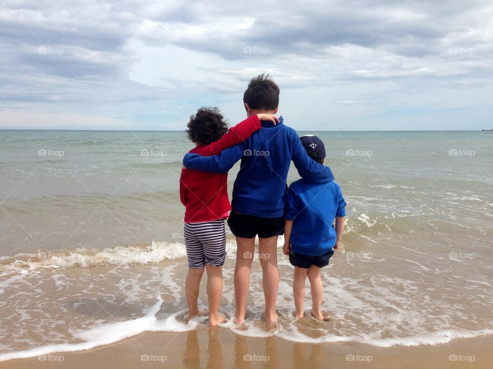 three children embraced looking at the sea in a cloudy day