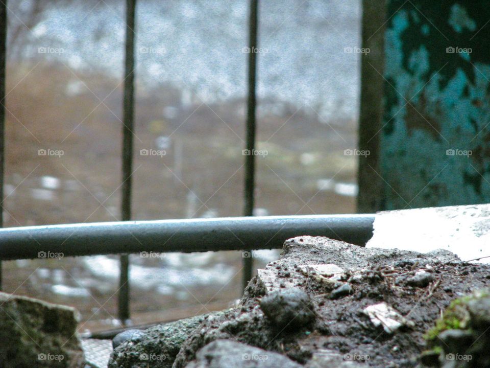 Close-up of a rough, uneven piece of rock or concrete in front, with horizontal pipes and vertical railings in back