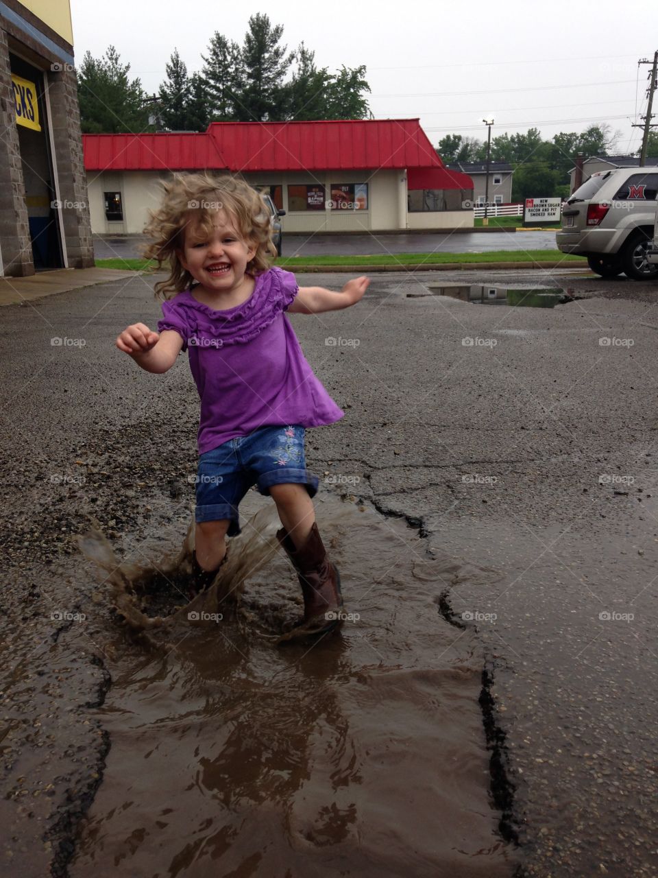 Rainy day fun in a mud puddle . Splashing in a mud puddle on a rainy day, and the joys of being three years old