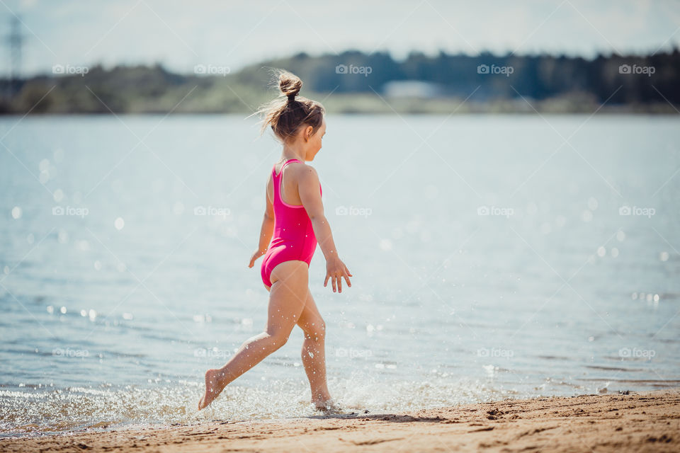 Little girl on lake coast at sunny evening. 