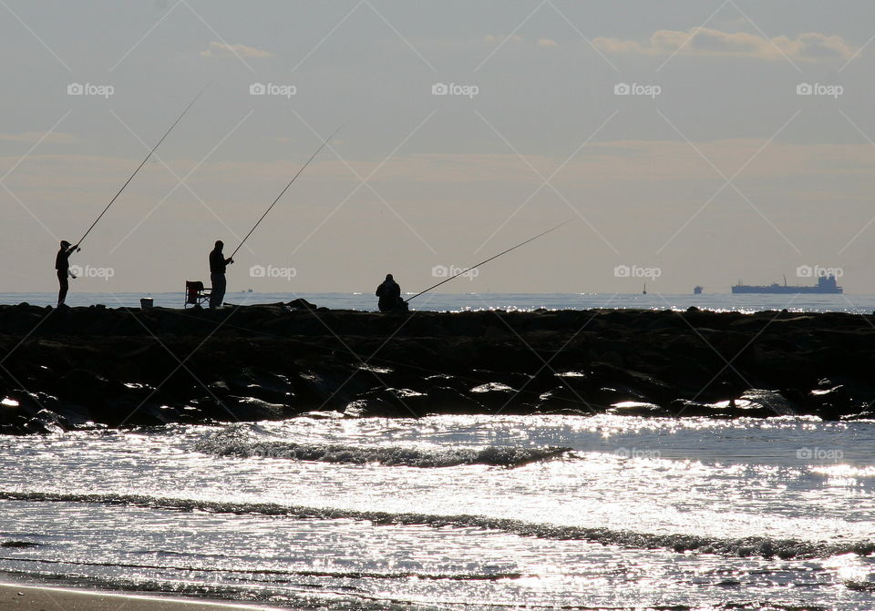 three fishermen silhouettes  in the  sun fishing in the mediterranea sea