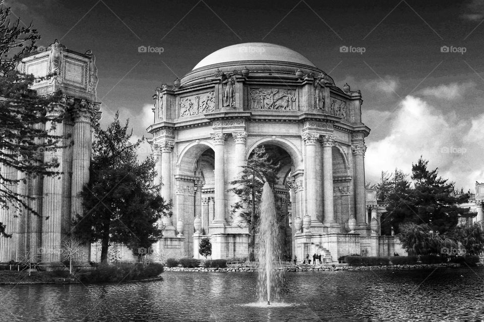 Vintage looking black and white image of the landmark Palace of Fine Arts in San Francisco California with the fountain rising through the lagoon on a warm sunny afternoon with clouds in the sky 