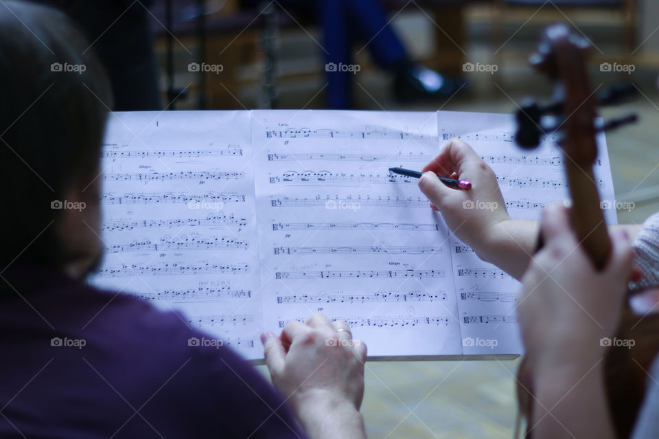 Musicians at rehearsal write pencil strokes in notes.  Violin.  Alto.