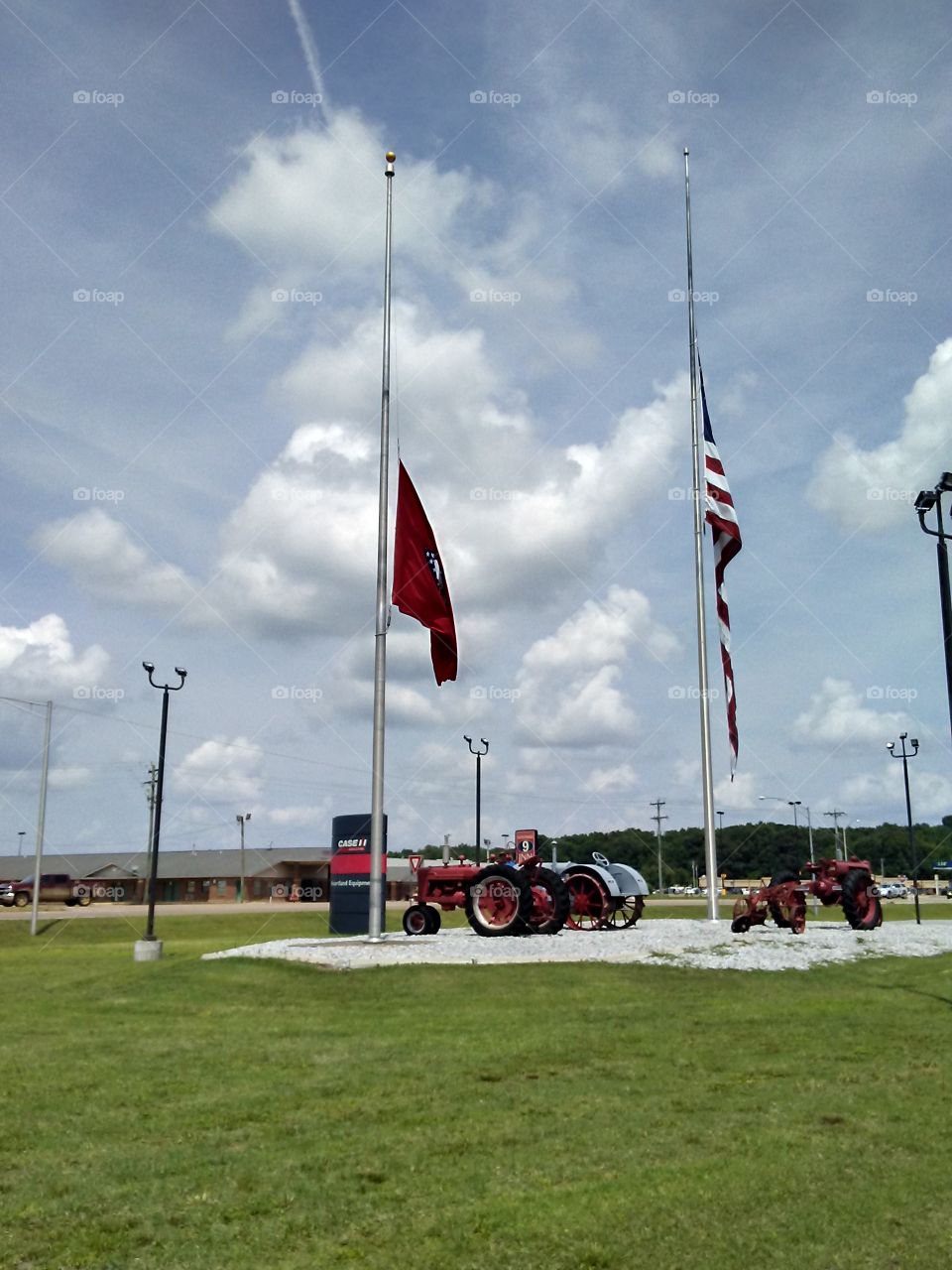 Arkansas and American flag at half staff with tractors under it gravel big blue sky scape