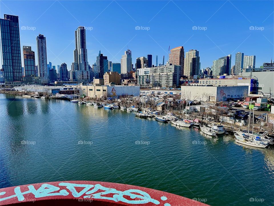This is “Newtown Creek“ seen from the „Pulaski Bridge“ that connects „Greenpoint“, Bklyn to LIC, Queens. Across the water you see LIC with all its boats and further remote „Manhattan“. 2024. Hypnotic Productions