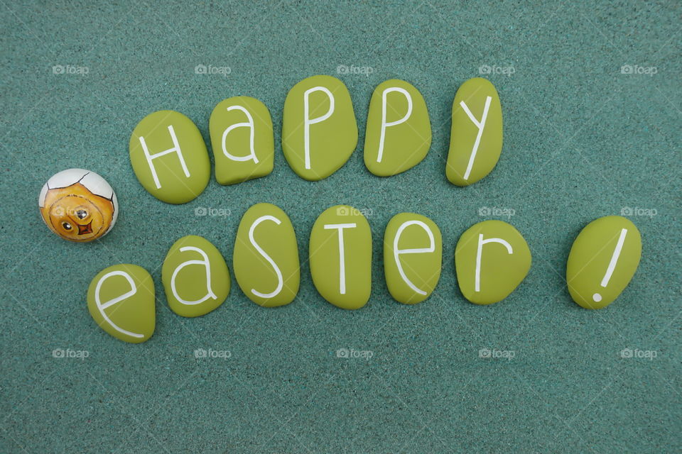 Happy Easter text composed over green sand with green painted stones and an egg design