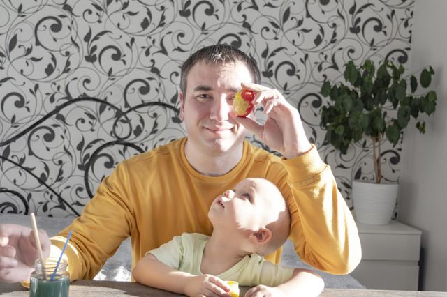 A little son and his father together in their free time paint Easter, chicken eggs with paints and brushes for the holiday.  A child and a man create a craft and natural product in their family business.