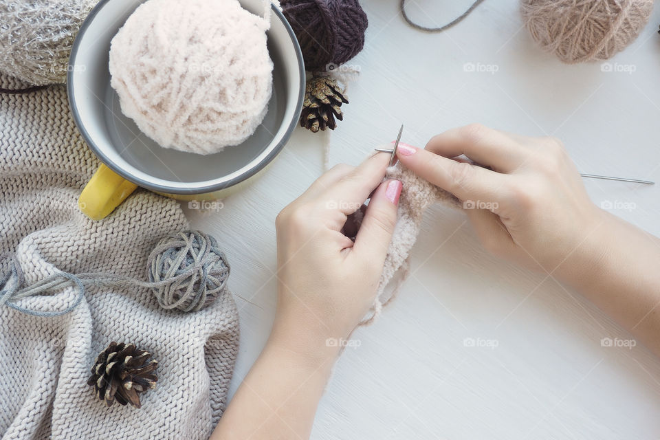 women's hands on a white table knitting needles . different balls of yarn and a knitted blanket.