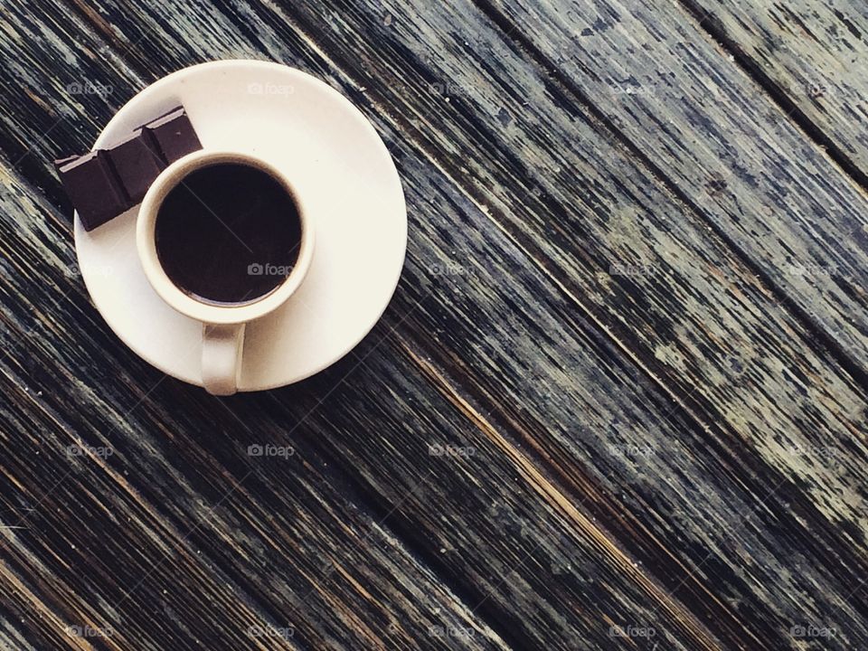 Cup of espresso and chocolate bar on wooden table