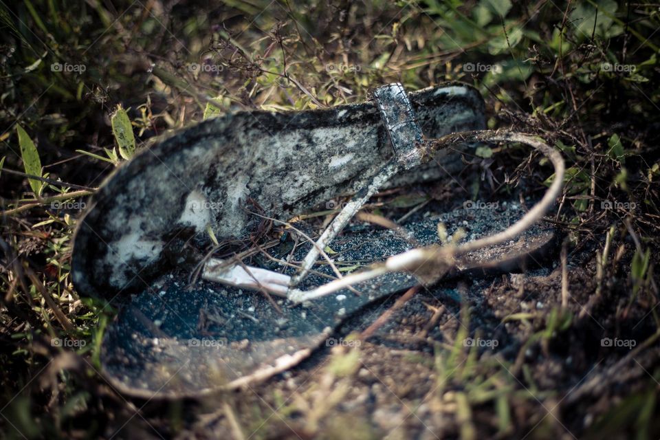 A pair of Flip Flops abandoned worn and weathered on the side of the road in the dirt and vegetation