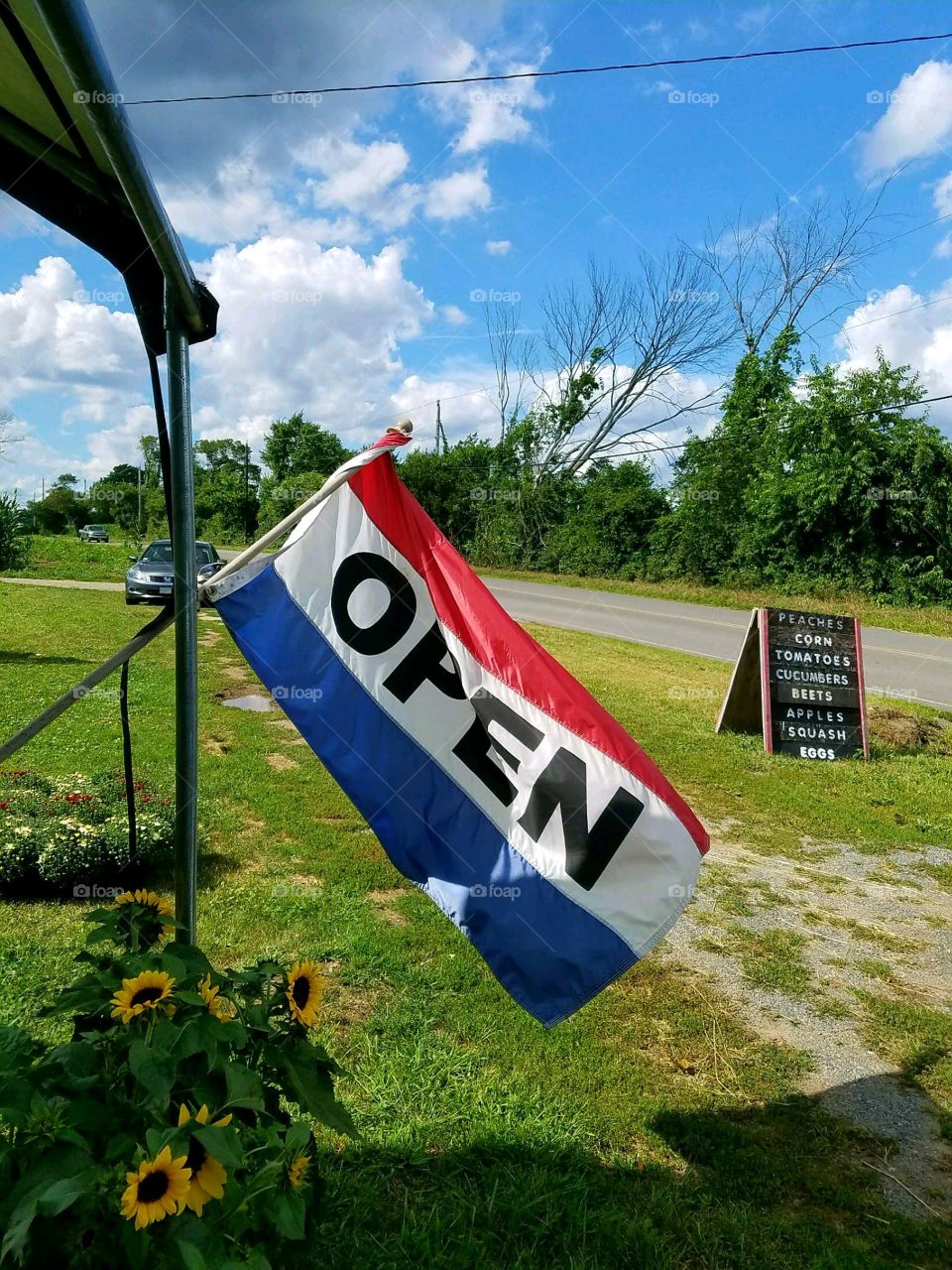 American Flag colors. Open for business on roadside farm stand. Red, white, blue on Open flag blowing in the wind. Farm roadside sign.