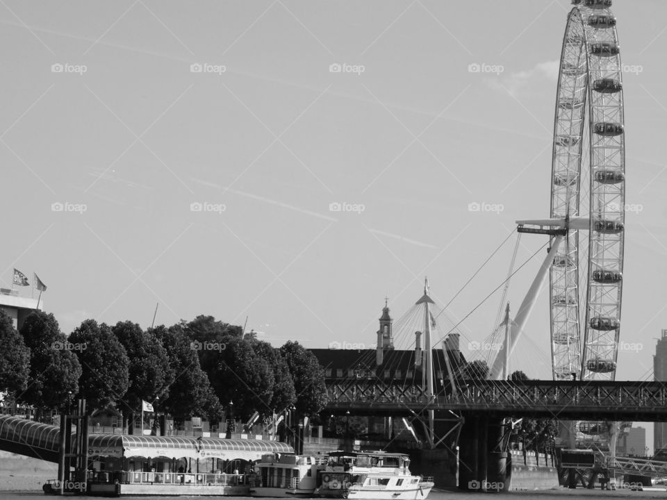 The London Eye towers above local historic buildings and boats on the Thames River in London on a sunny summer day. 