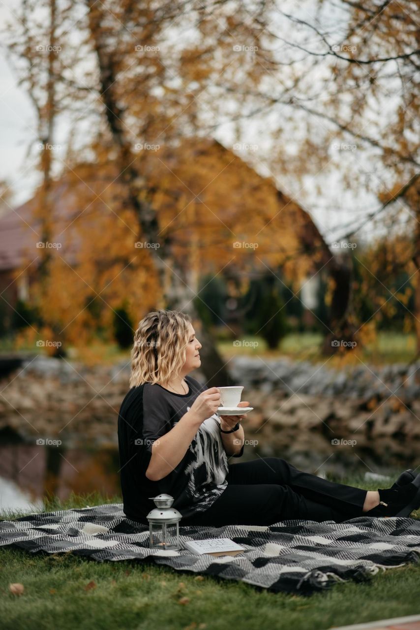 Autumn tea party and picnic of a young woman in an autumn park near the lake