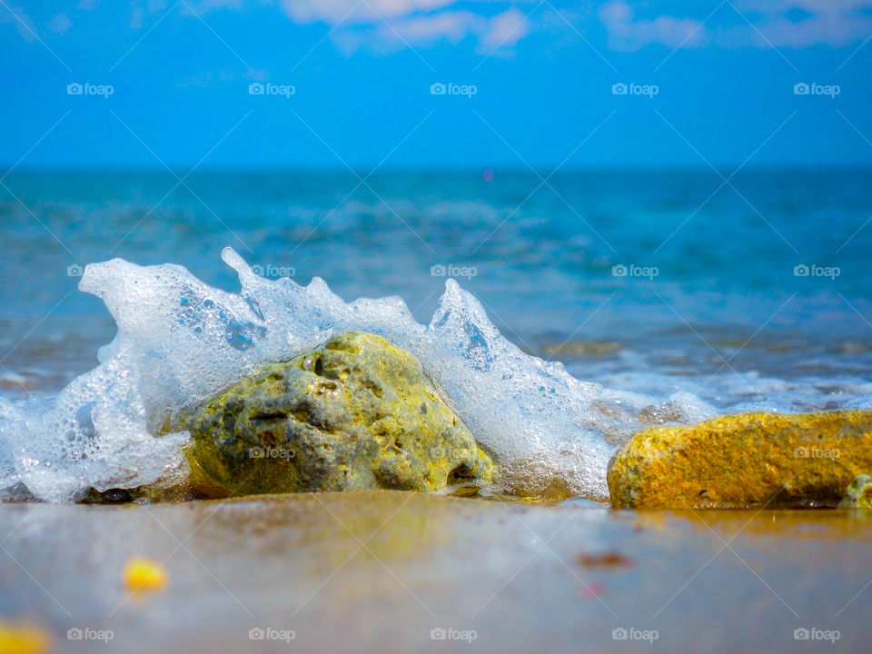 Splash of a sea wave on a stone on a sandy beach in the bright sun