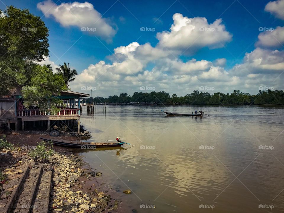 Long-tail fishing boat in the Tapi River under cloudy blue sky in Surat Thani, southern Thailand