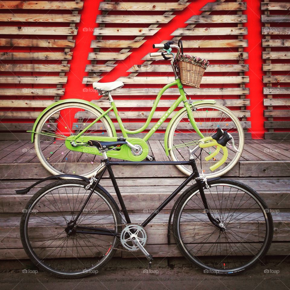 Green electra amsterdam city bicycle and black singlespeed soviet commuter bicycle with a front bicycle rack and yellow grips in front of wooden wall in Moscow, Russia