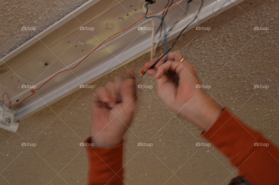 Man’s hands doing electrical work above head 
