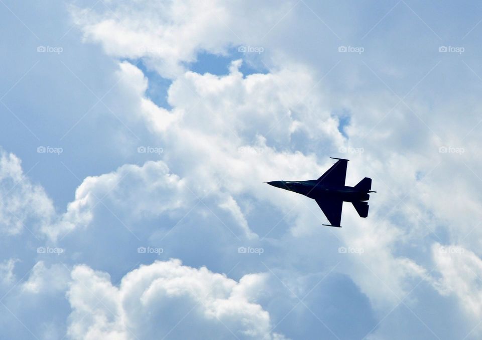 Jet silhouette against blue sky and white fluffy clouds